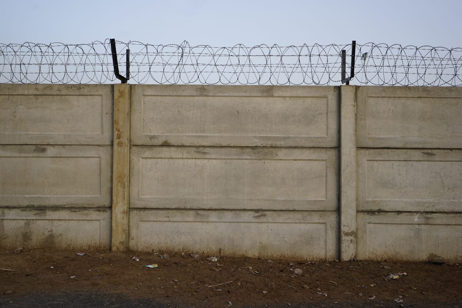 Plain grey precast compound wall topped with razor wire fencing
